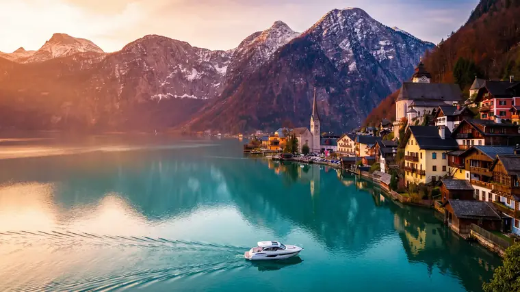 Motorboot auf einem türkisen Alpensee, am Ufer ein Ort mit Kirchturm vor verschneiten Bergen