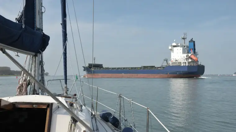 Blick von einer kleinen Segelyacht auf ein deutlich größeres Frachtschiff, das den Kurs kreuzt