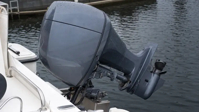 Ein nach oben gekippter Außenborder am Heck eines weißen Motorboots im Hafen, der untere Teil mit dem Getriebegehäuse hängt frei über dem Wasser