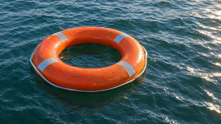 Geschlossener orangefarbener Rettungsring auf leicht bewegtem blaugrünem Wasser.