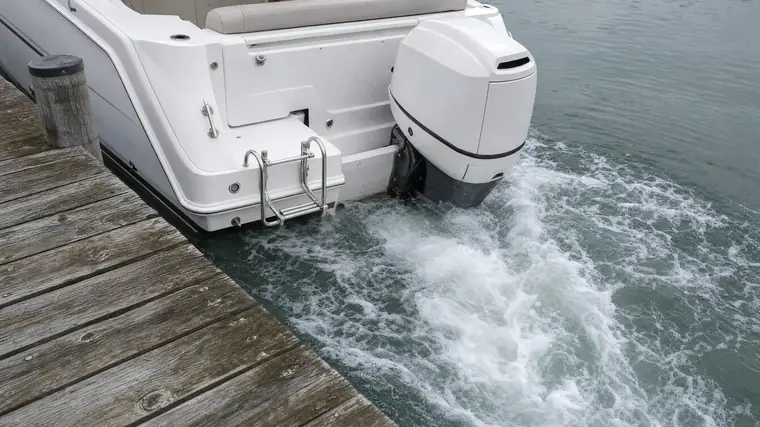 Heck eines Motorboots am Steg: das Schraubenwasser kocht seitlich am Rumpf hoch und drückt das Heck zur Seite