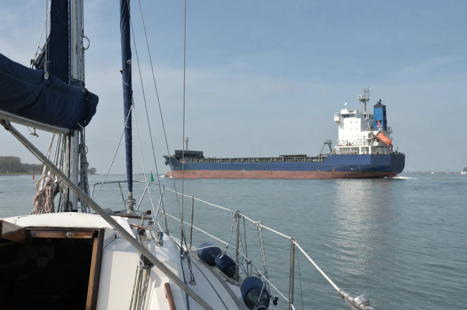 Blick von einer kleinen Segelyacht auf ein deutlich größeres Frachtschiff, das den Kurs kreuzt