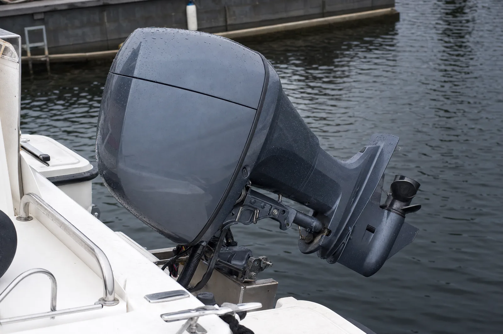 Ein nach oben gekippter Außenborder am Heck eines weißen Motorboots im Hafen, der untere Teil mit dem Getriebegehäuse hängt frei über dem Wasser