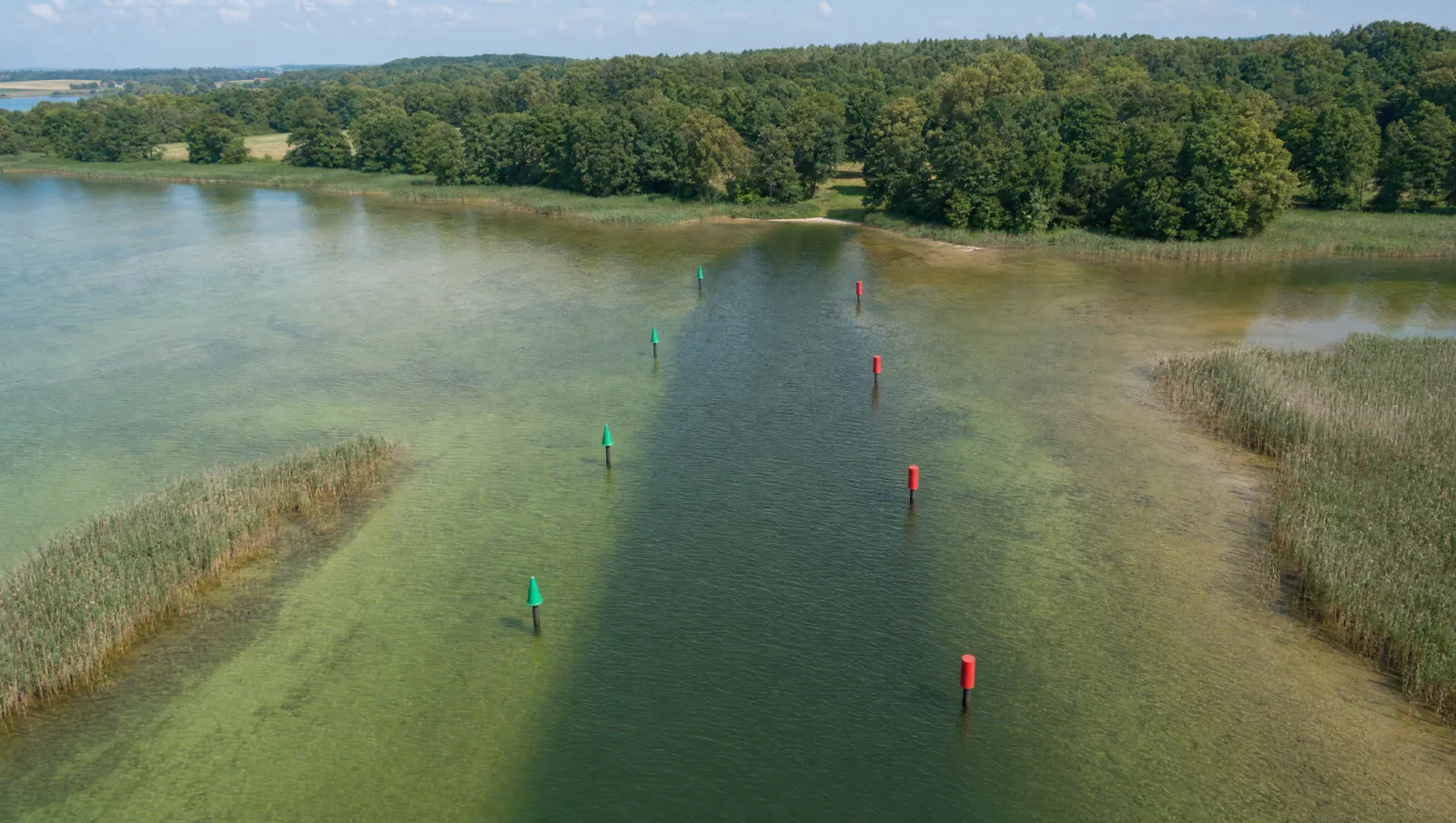 Luftbild einer betonnten Fahrrinne auf einem See: grüne Kegeltonnen auf der einen, rote Stumpftonnen auf der anderen Seite, dazwischen dunkleres tiefes Wasser