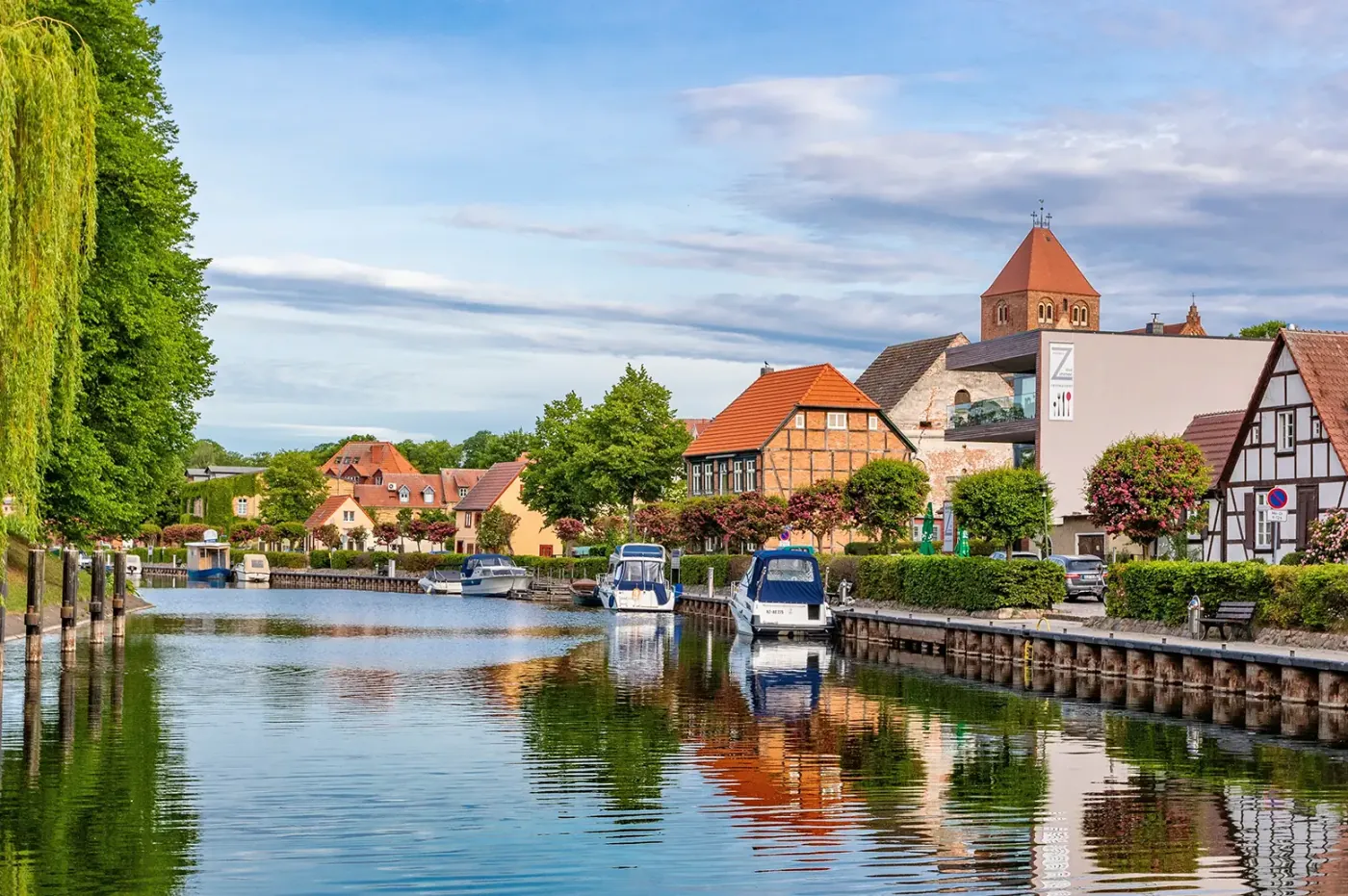 Hafenpromenade mit festgemachten Motorbooten und Fachwerkhäusern an einem Kanal in der Mecklenburgischen Seenplatte