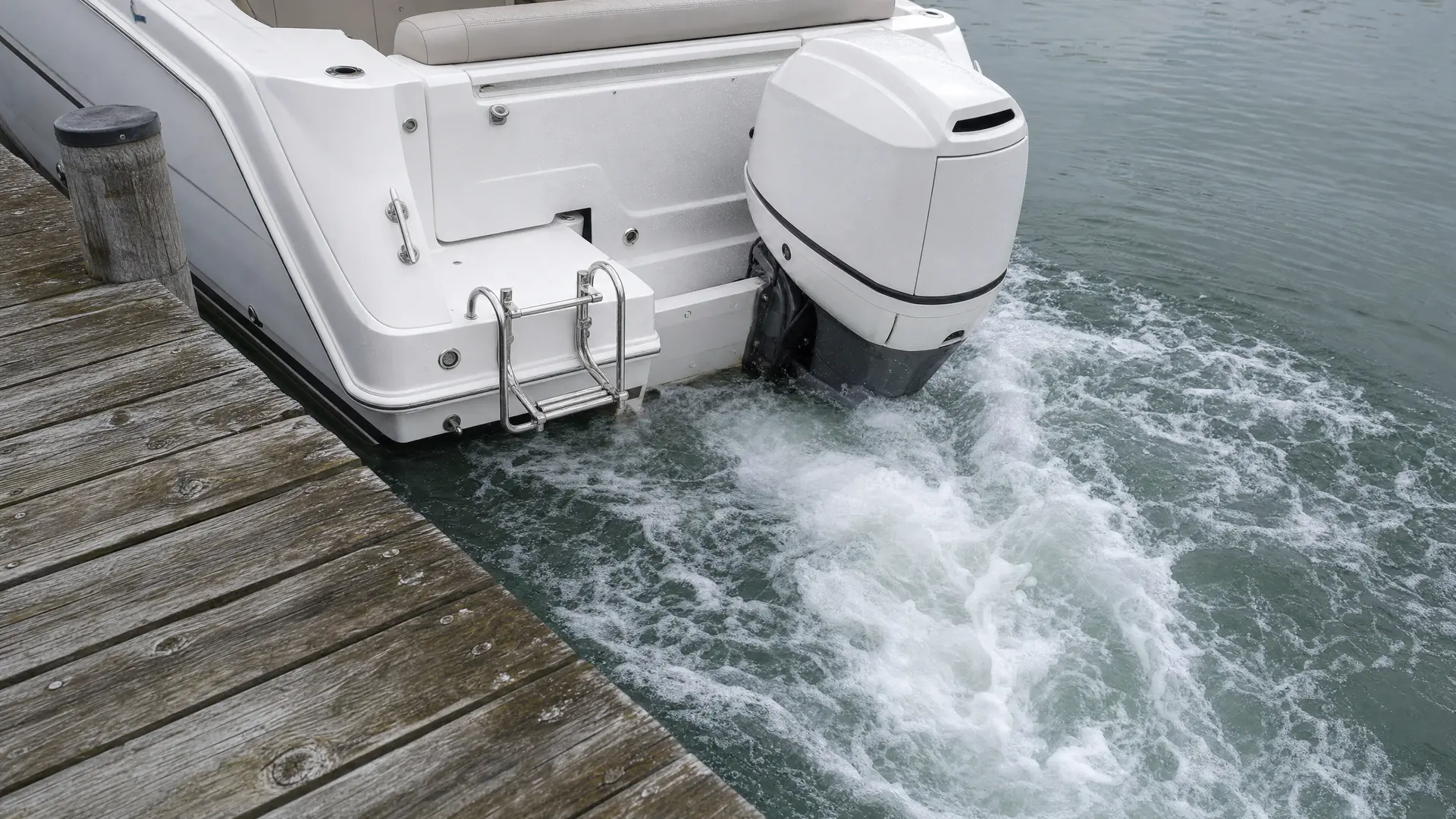 Heck eines Motorboots am Steg: das Schraubenwasser kocht seitlich am Rumpf hoch und drückt das Heck zur Seite