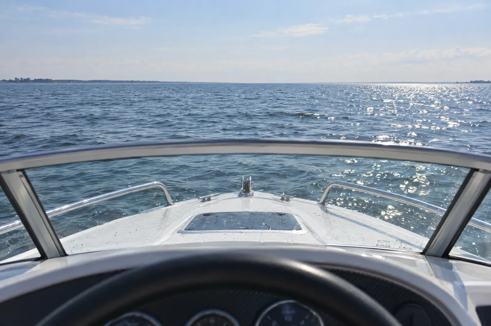 Blick vom Steuerstand eines Motorboots über den Bug auf die offene Ostsee, die Küste nur noch als flacher Streifen am Horizont