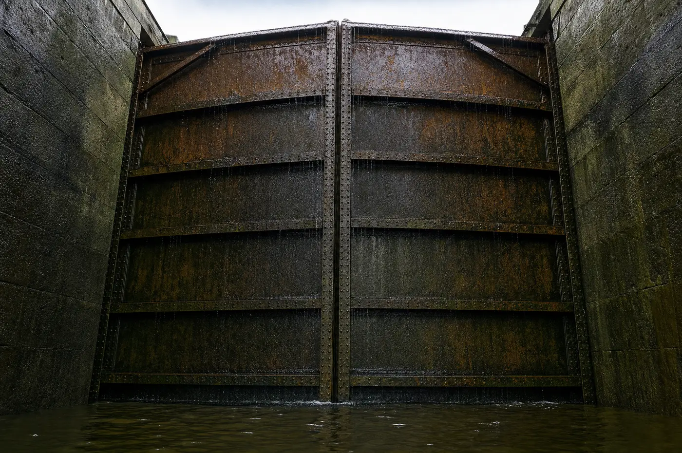 Stählernes Schleusentor von innen aus der Kammer gesehen, genietete Platten mit Rost und Algen, an der Oberkante läuft noch Wasser herunter
