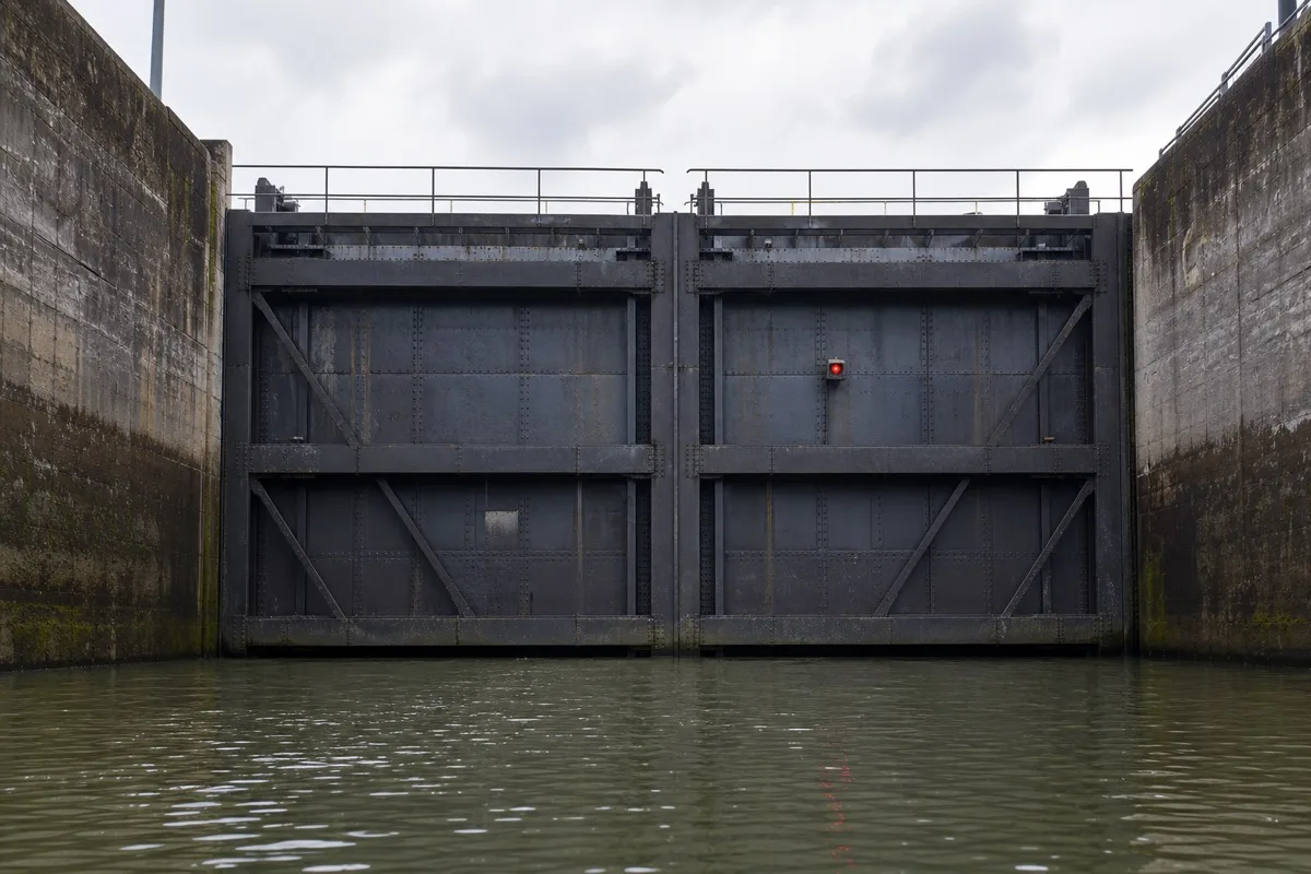 Geschlossenes stählernes Schleusentor mit rotem Signallicht, von der Wasserseite aus zwischen den Betonwänden der Schleusenkammer