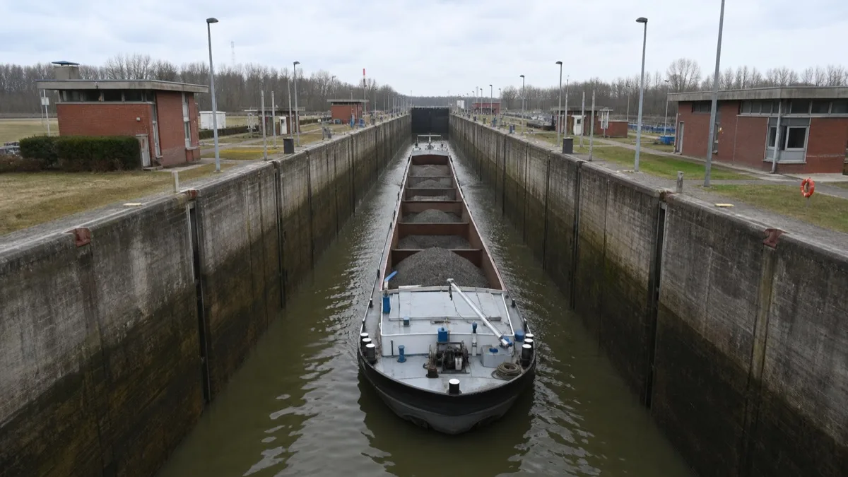 Große Kanalschleuse von der Brücke am Kammerkopf aus, ein beladenes Frachtschiff liegt in der gefüllten Kammer zwischen roten Betriebsgebäuden