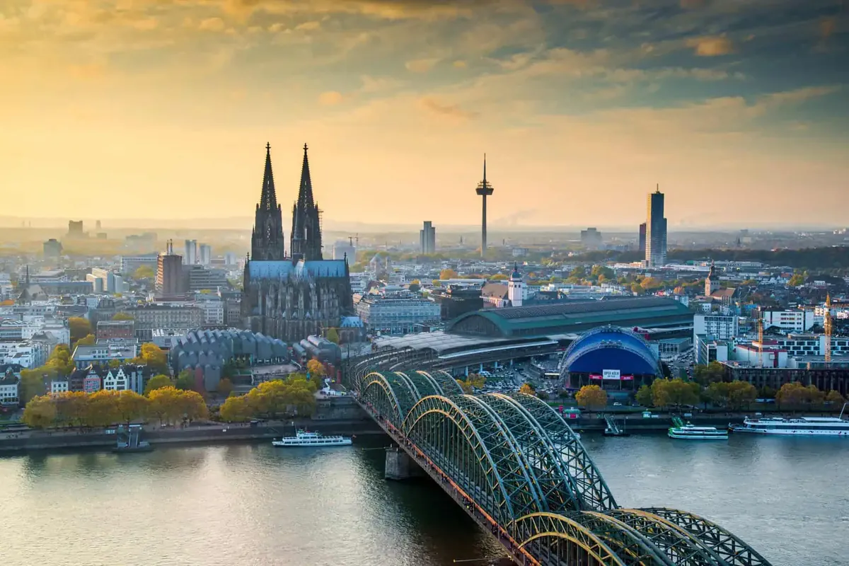Köln im Abendlicht von oben: Kölner Dom, Hohenzollernbrücke über den Rhein und Ausflugsschiffe am Ufer