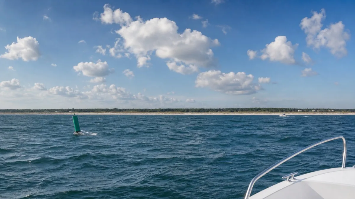 Blick vom Bug eines kleinen Motorboots über offenes Ostseewasser auf eine grüne Fahrwassertonne