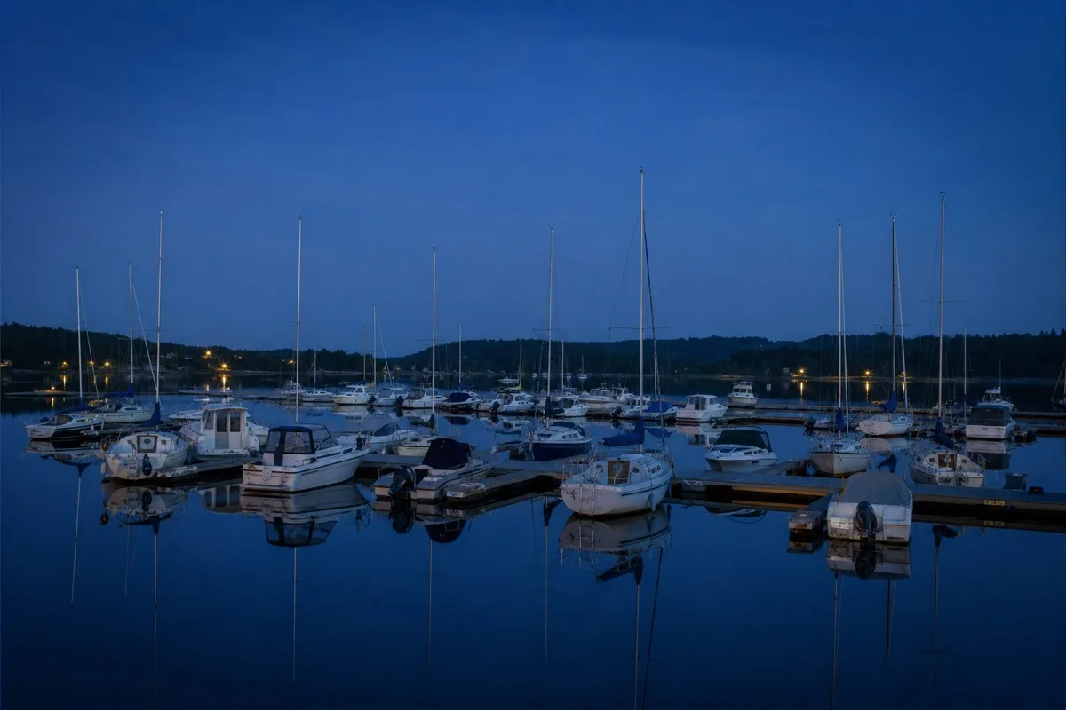 Geschütztes Hafenbecken zur blauen Stunde, rund dreißig Sport- und Segelboote an Schwimmstegen, die Masten spiegeln sich im stillen Wasser